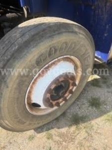 Wheel with Goodyear tire and white rim on a blue International truck, visible rust around hub, dirt and grass nearby.