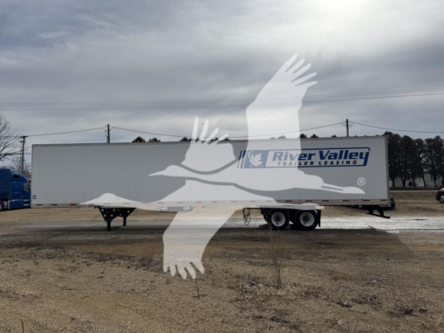 Trailer side of a used 2017 utility dry van with River Valley trailer leasing logo on the side and a white cab-over truck in the background.