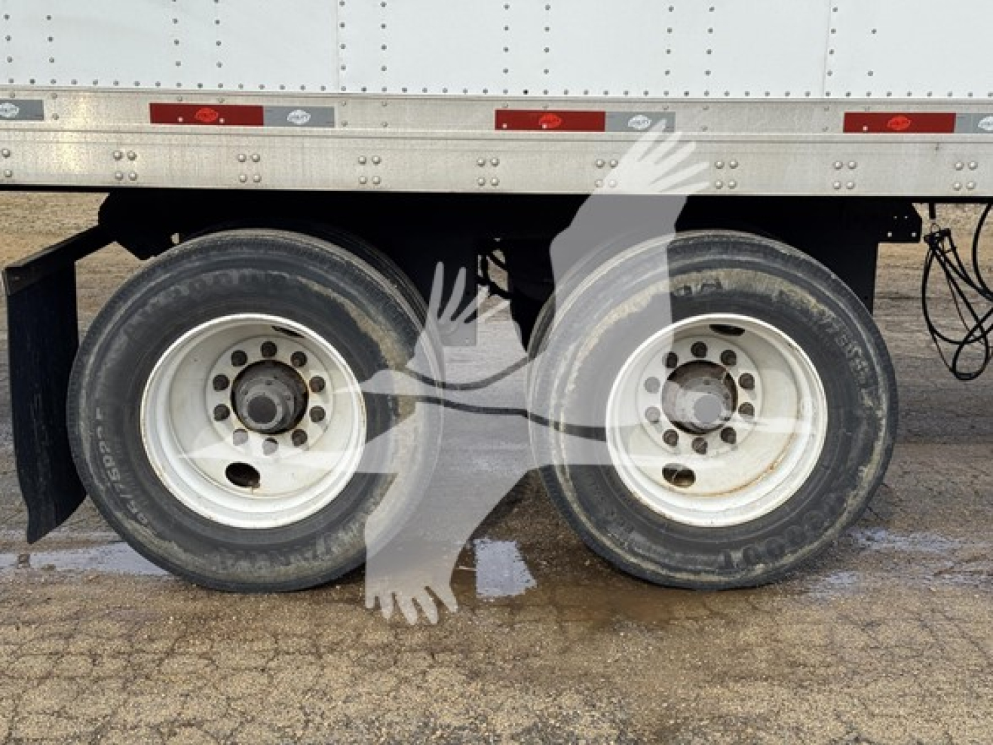 Dual rear wheels of a utility dry van trailer showing dual tires and undercarriage; side of trailer with reflective strips.