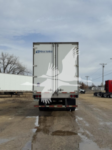 Rear view of a 2017 Utility dry van trailer showing two doors with Rivian stickers and taillights, on a muddy lot.