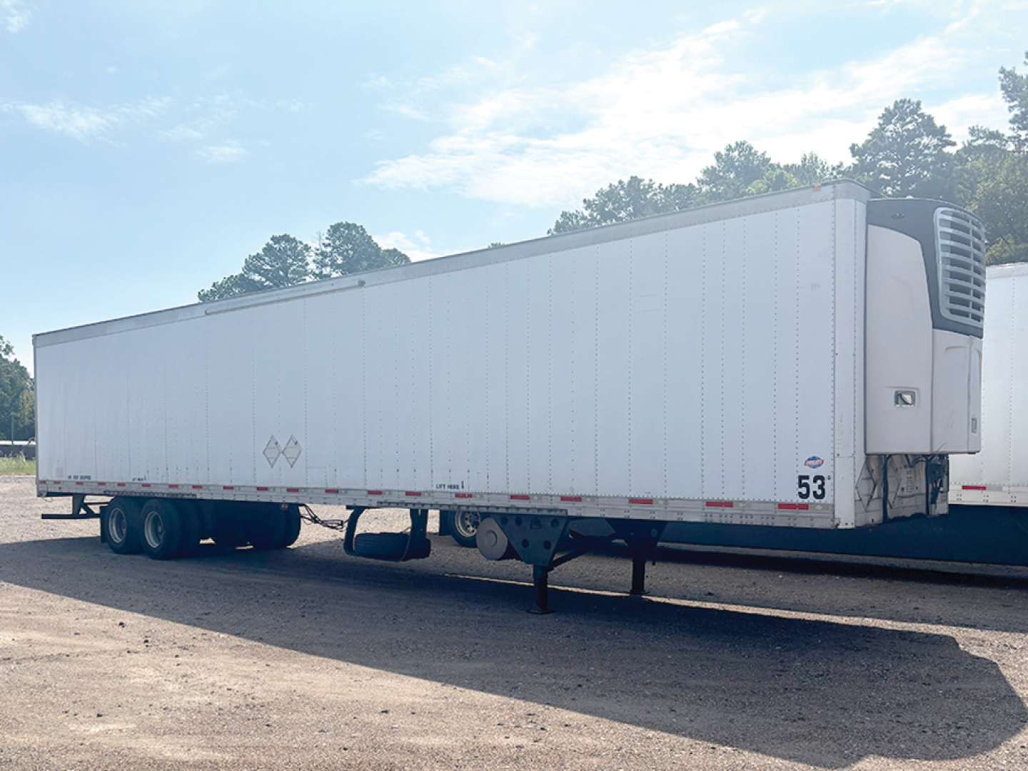 Trailer side view showing a white refrigerated trailer with front refrigeration unit and landing gear.