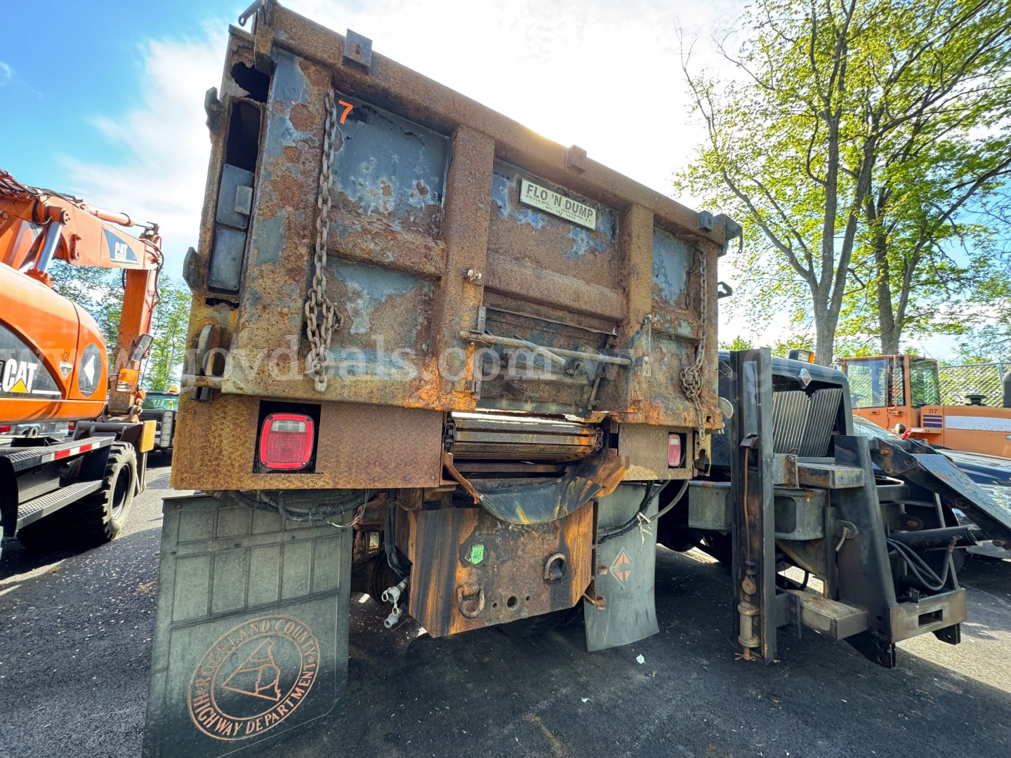 Dump truck bed of a 2004 International 5600i with rusted metal, rear view showing tailgate, chain, lights, and hydraulic components.