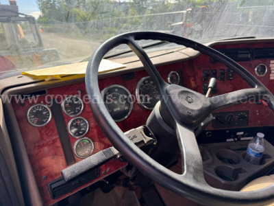 Cab interior of a 2004 International 5600i dump truck showing steering wheel, multiple gauges, and dashboard with red paneling.