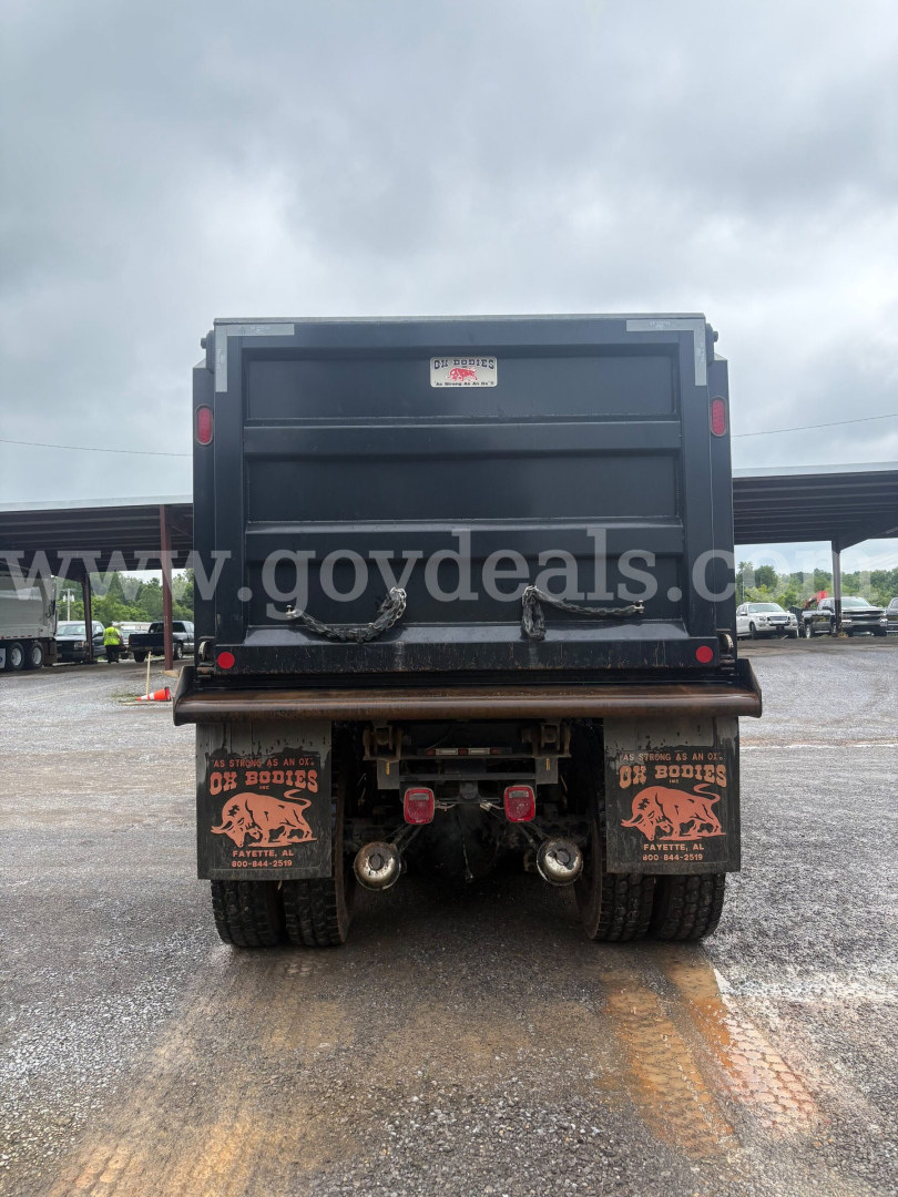 Rear view of a 2025 Peterbilt 377 dump truck showing dump bed and rear axles with dual tires; mud flaps with logos; platform and hitch area visible.