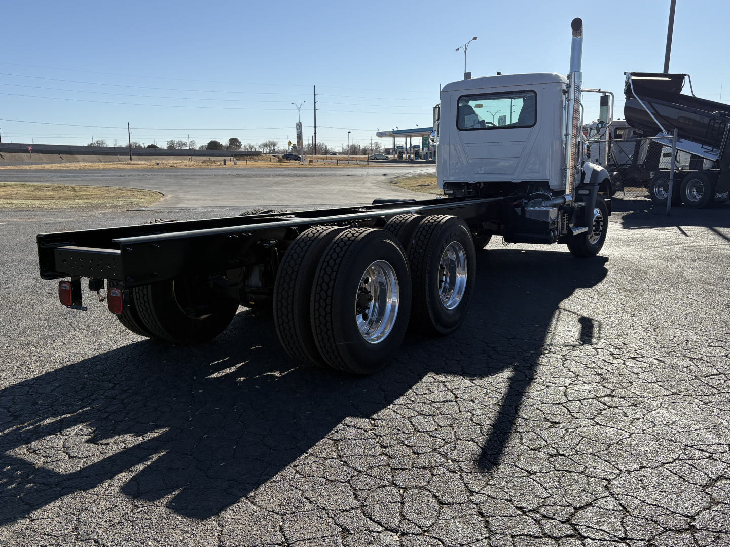 Mack GR64B chassis side view showing bare frame and rear tandem axles with white cab in background.
