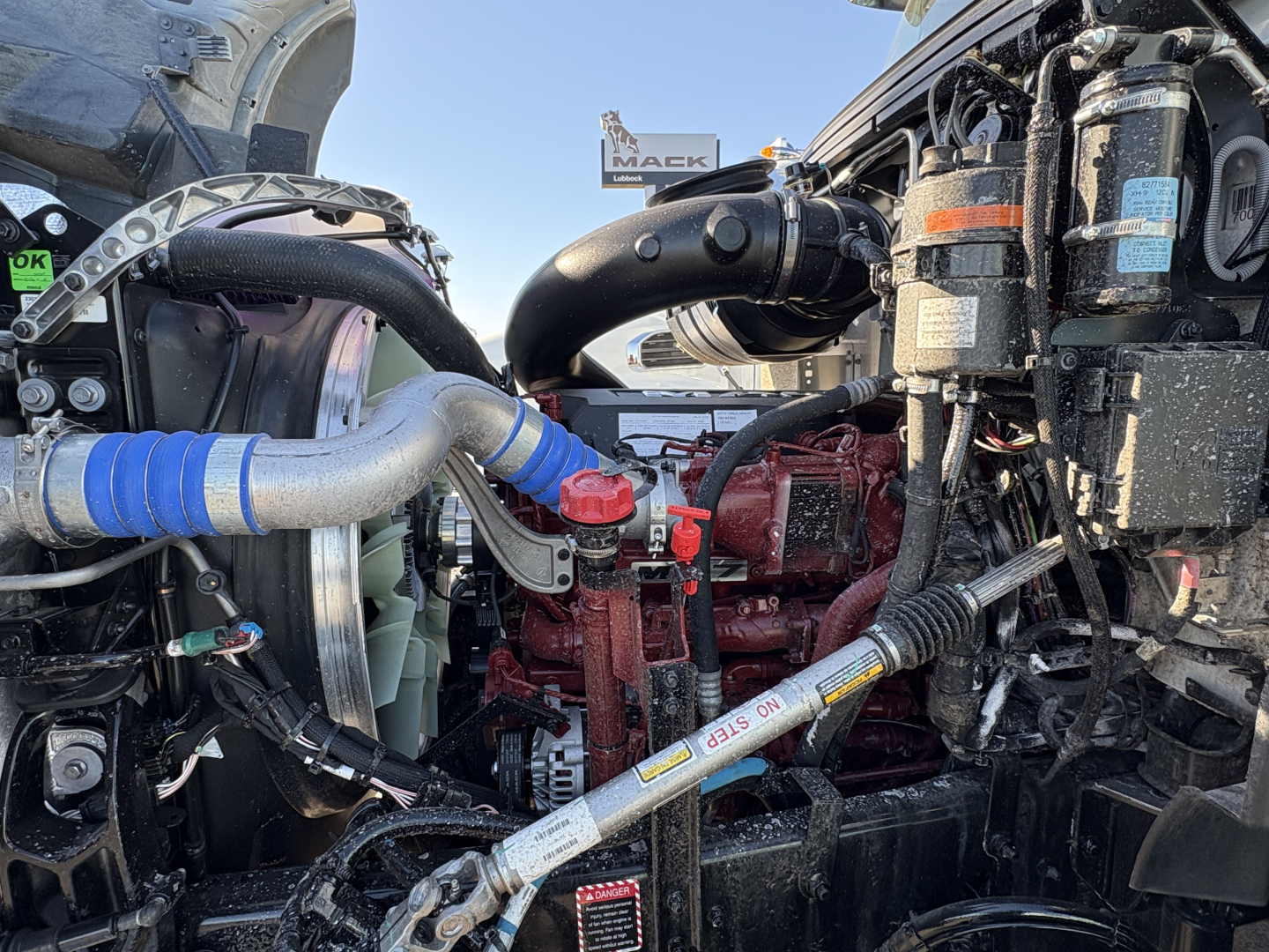 Mack GR64B engine bay showing diesel engine components, hoses, and labels visible on a winch-equipped truck.