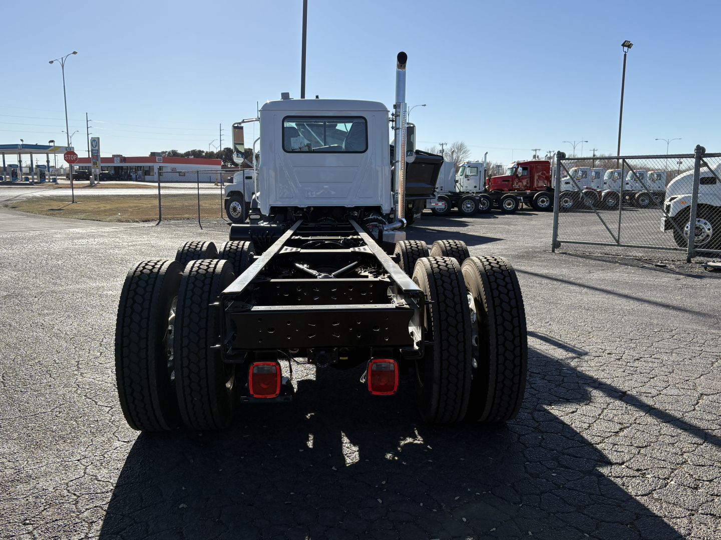 Rear view of a white 2027 Mack GR64B truck chassis showing dual rear dual tires and fifth wheel missing cabin, in a truck yard.