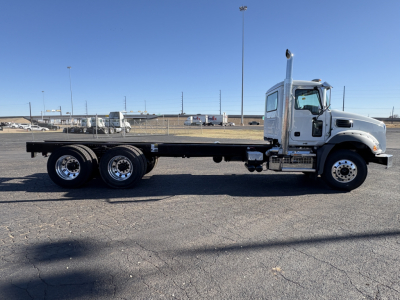 Side view of a white Mack GR64B truck with a long flatbed chassis and multiple rear wheels.
