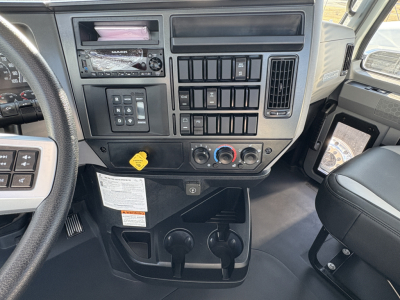 Dashboard of a Mack GR64B truck showing radio, controls, vents, and two cupholder areas; various switches and knobs visible on center console.