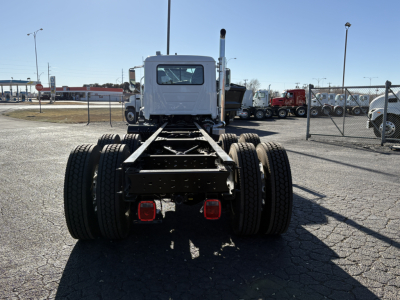 Rear view of a white 2027 Mack GR64B truck chassis showing dual rear dual tires and fifth wheel missing cabin, in a truck yard.