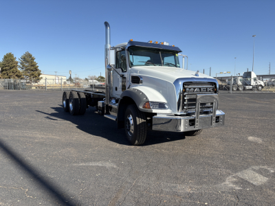 Truck chassis with front cab of a Mack GR64B, silver exterior, chrome bumper, tall exhaust stack, daytime lot view.
