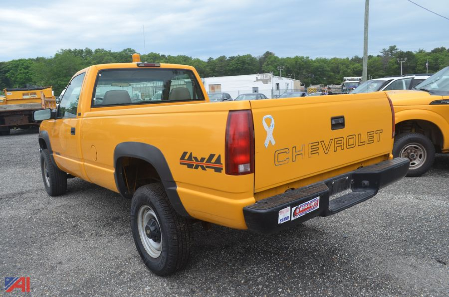 Yellow 1997 Chevrolet C/K 2500 pickup truck seen from rear-left side with 4x4 decal, tailgate Chevrolet lettering, white ribbon sticker, black bumper, pickup bed, in a lot.