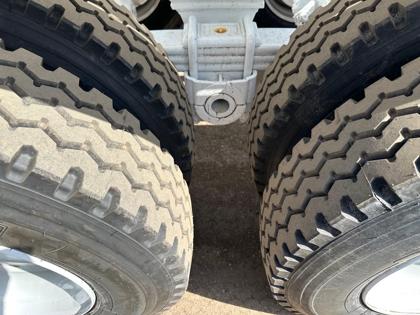 Bottom dump trailer axle view showing dual tires and central hitch area with suspension member.