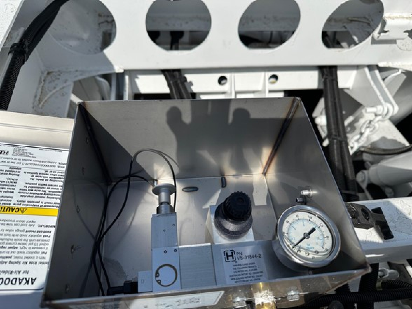 Dump truck trailer hopper with gauge and control box inside a stainless metal enclosure showing a round pressure gauge and wiring.