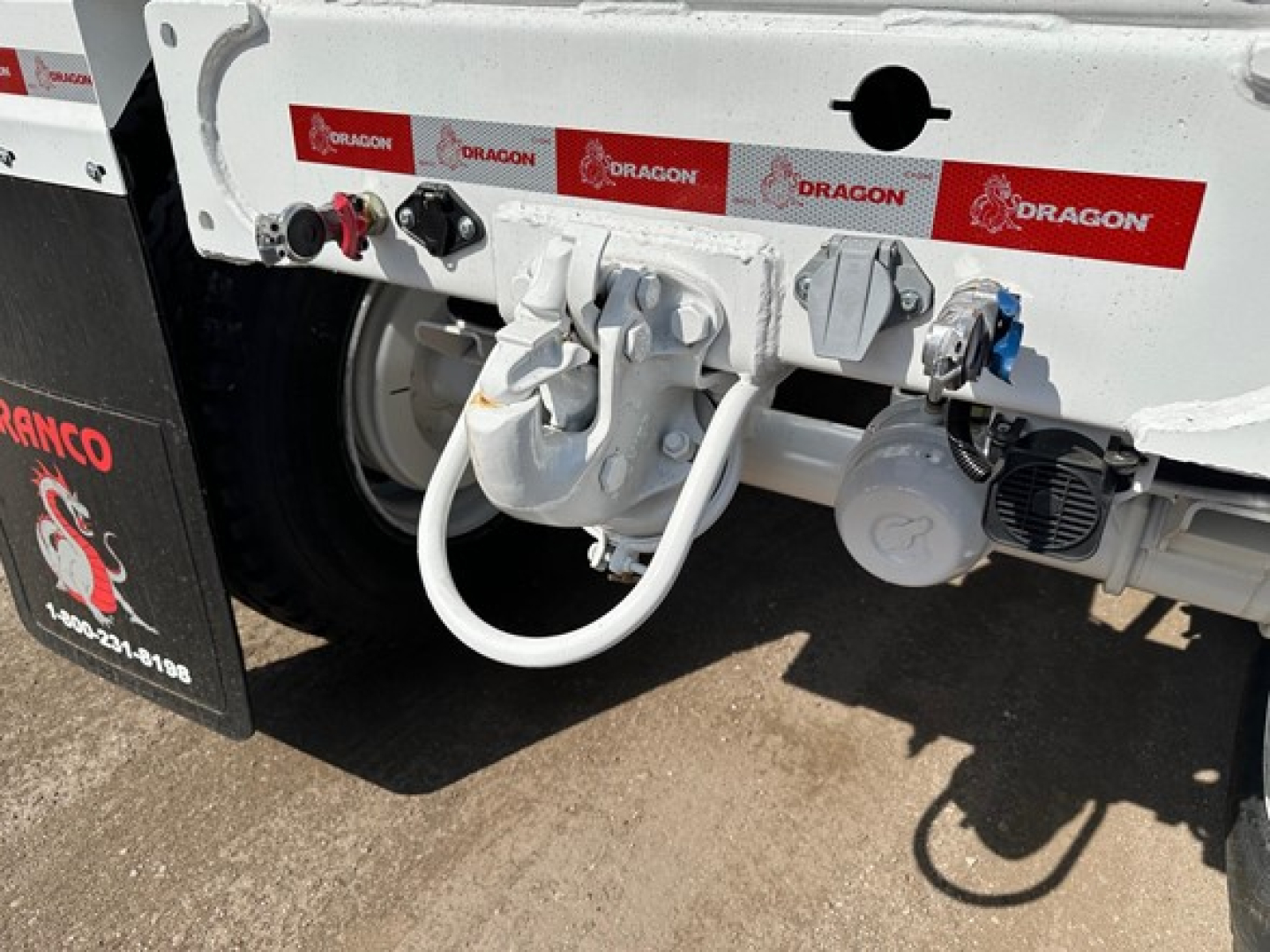 Trailer rear showing coupling hitch and white hoses with visible labels: 'DRAGON' repeated on red and white stickers along the bumper.