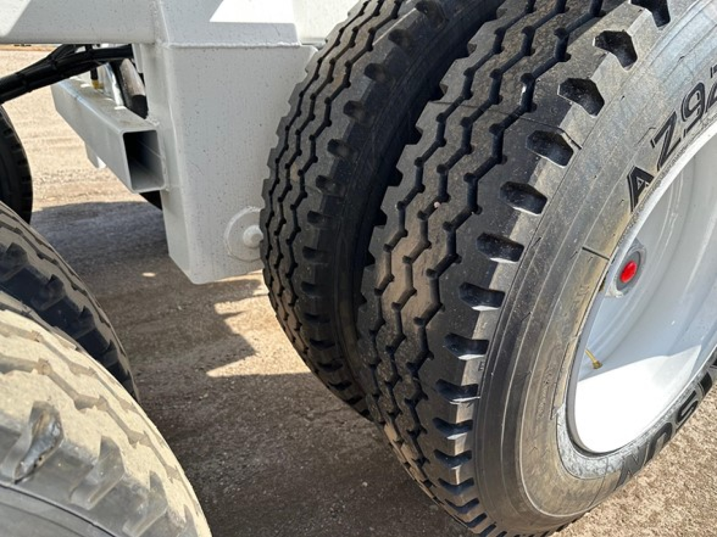 Trailer wheel and rubber tire with tread pattern visible; section of white dump trailer chassis in background.