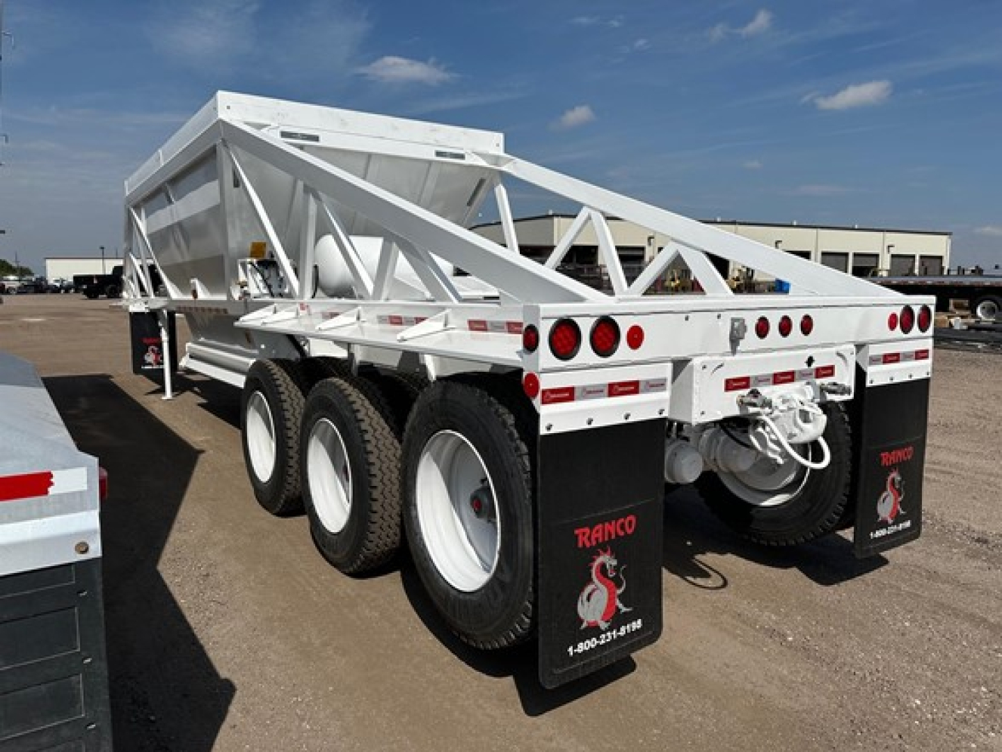 Dump trailer showing tri-axle bottom dump with white painted metal frame and dual rear mud flaps, Ranco branding on mud flaps.