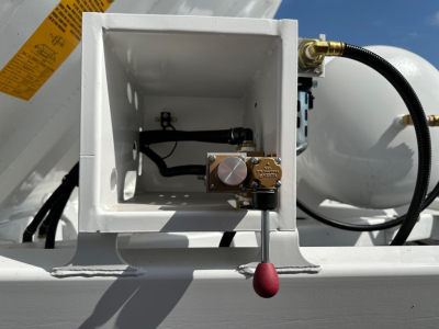 Bottom dump trailer component with control valve and hydraulic lines in an open square housing, brass valve body, red knob actuator, and hydraulic hose.