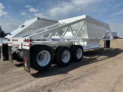 Bottom dump trailer with tri-axle configuration, white metal structure, rear deck and dual rear ramps. Visible label area includes no legible text beyond branding on mud flaps.