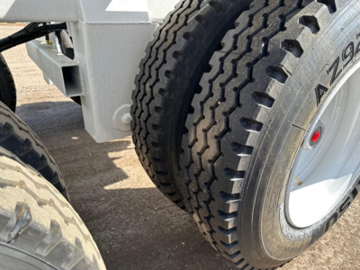Trailer wheel and rubber tire with tread pattern visible; section of white dump trailer chassis in background.