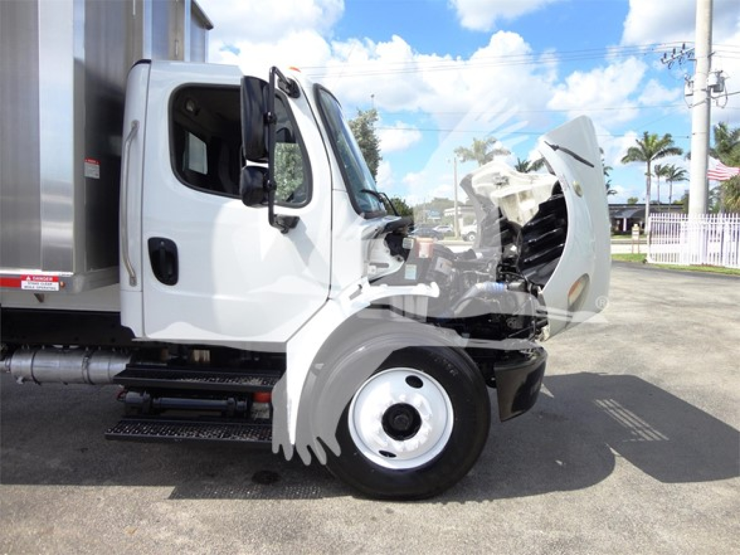 Truck cab of a Freightliner M2 106 with hood open showing front engine area and side view; white exterior; chipper truck configuration.