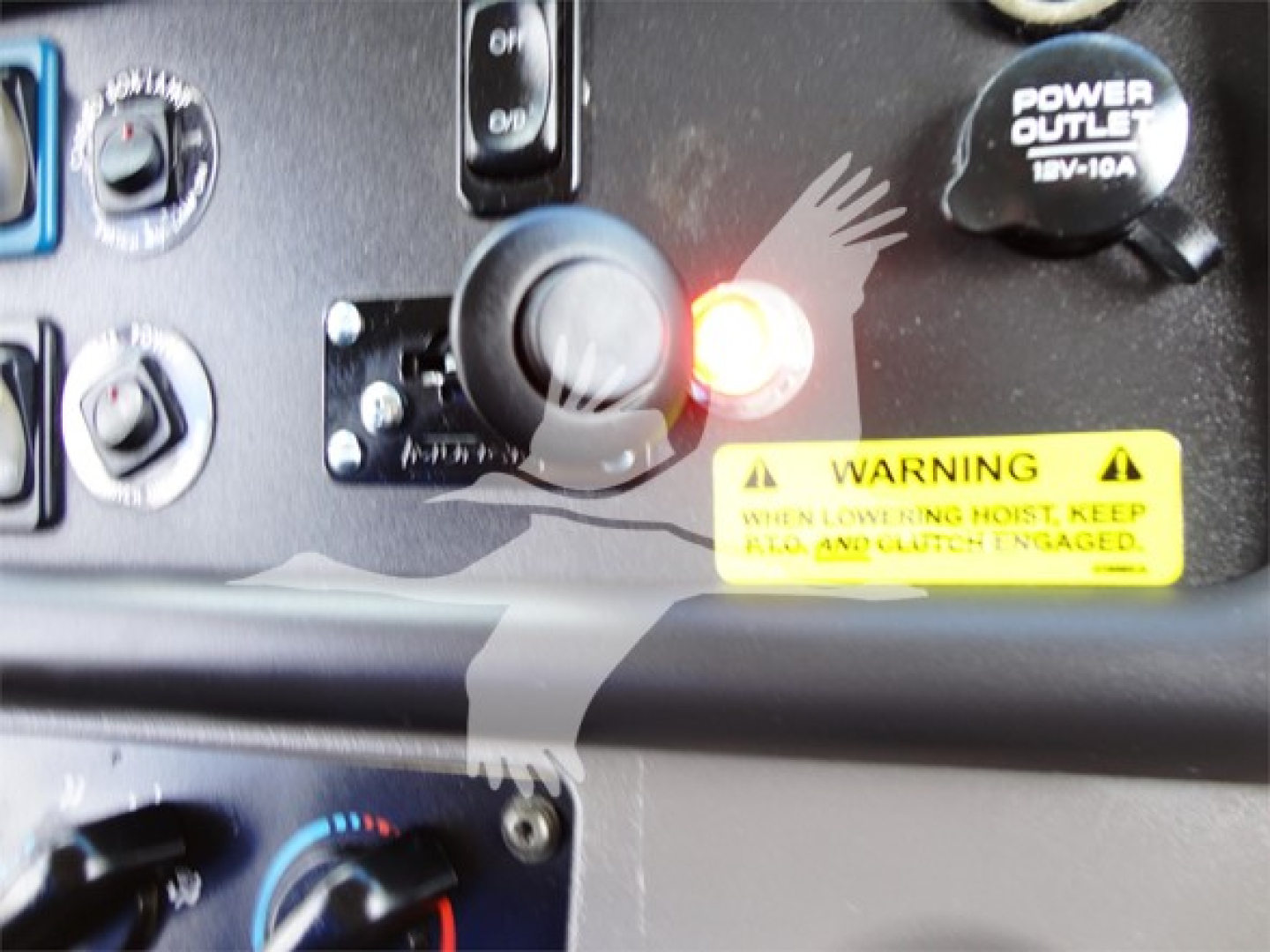 Dashboard area of Freightliner M2 106 showing ignition/coating switches and warning label, with power outlet and control knobs visible.