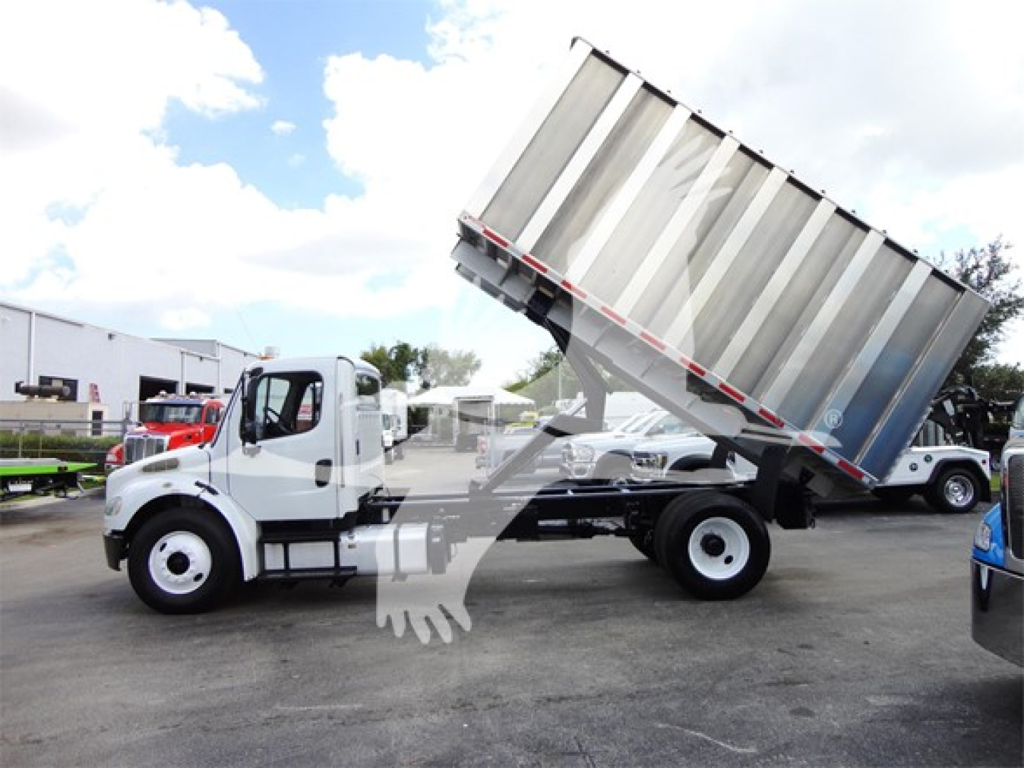 2014 Freightliner M2 106 truck with tilted dump bed in a dealership lot, side view showing cab and chassis