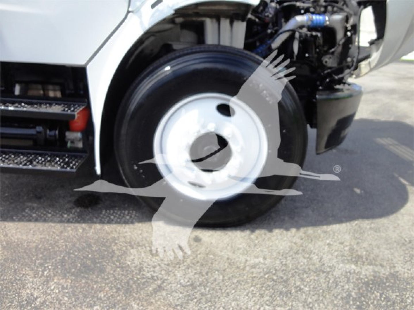 Front wheel well and engine bay of a Freightliner M2 106 truck showing front tire and partial chassis components.