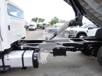 Freightliner M2 106 chassis/cab side view showing fuel tank and chassis frame, with truck yard in background.