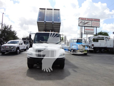 Front view of a white 2014 Freightliner M2 106 dump truck with the dump bed raised, in a dealership lot with other trucks visible.