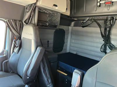 Freightliner Cascadia126 sleeper cab interior showing captain seats, overhead storage, and sleeping berth with blue mattress pad.