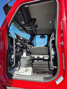Cab interior of a red Western Star 47X truck showing the driver seat, steering wheel, dashboard, and entry area.