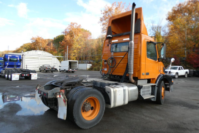 Volvo VNM42T cab-over tractor showing side view with intake stack and orange exterior, rear chassis and fuel tanks visible.