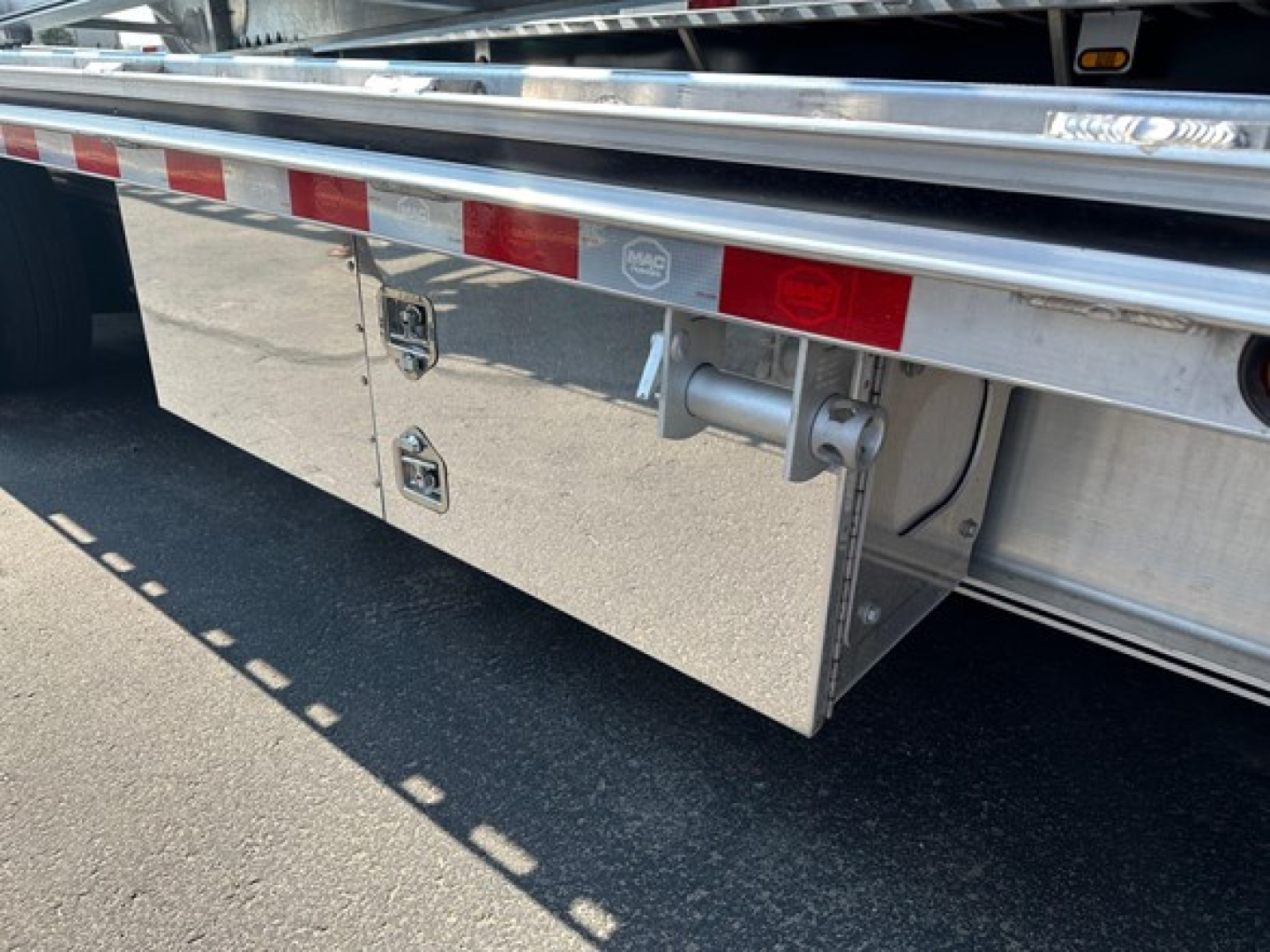Mac trailer side showing polished aluminum storage boxes and hitch mount with reflective tape.