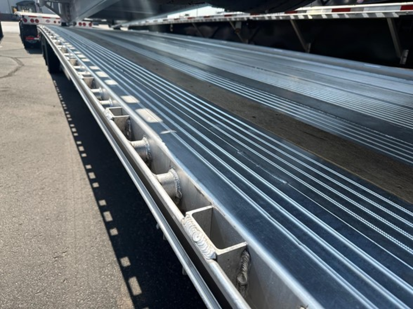 Flatbed trailer deck with metal ribbed surface and side rails, long perspective showing load floor and support beams.