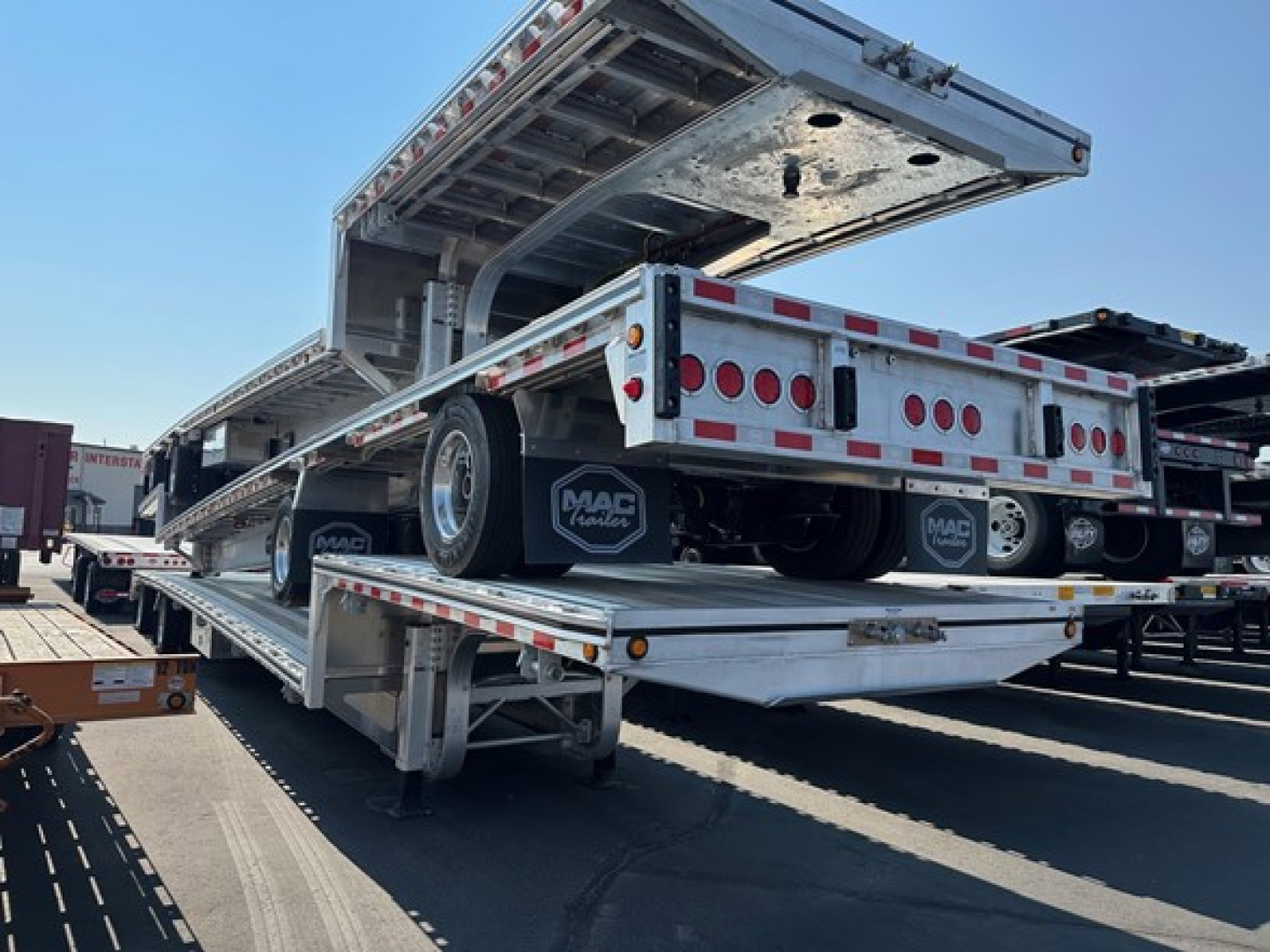 Mac drop deck trailer on a multi-axle flatbed with open hydraulic ramp gate and rear lighting.
