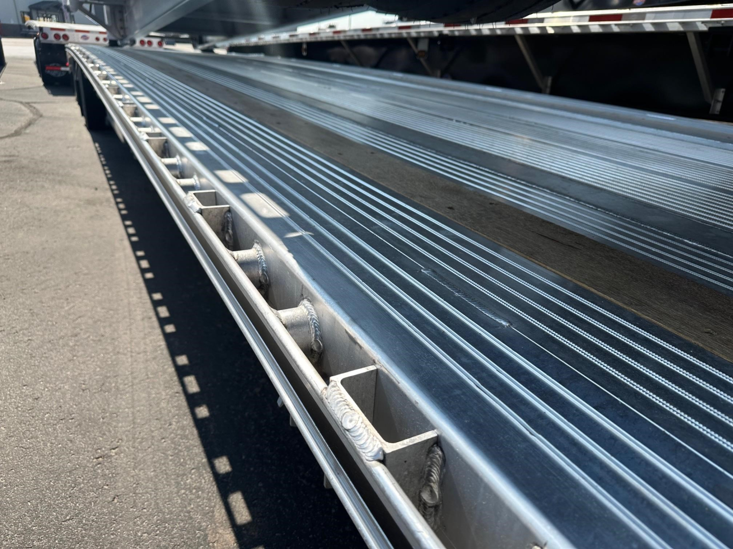 Close-up of a Mac drop deck trailer bed with ribbed aluminum surface and side guide rails.