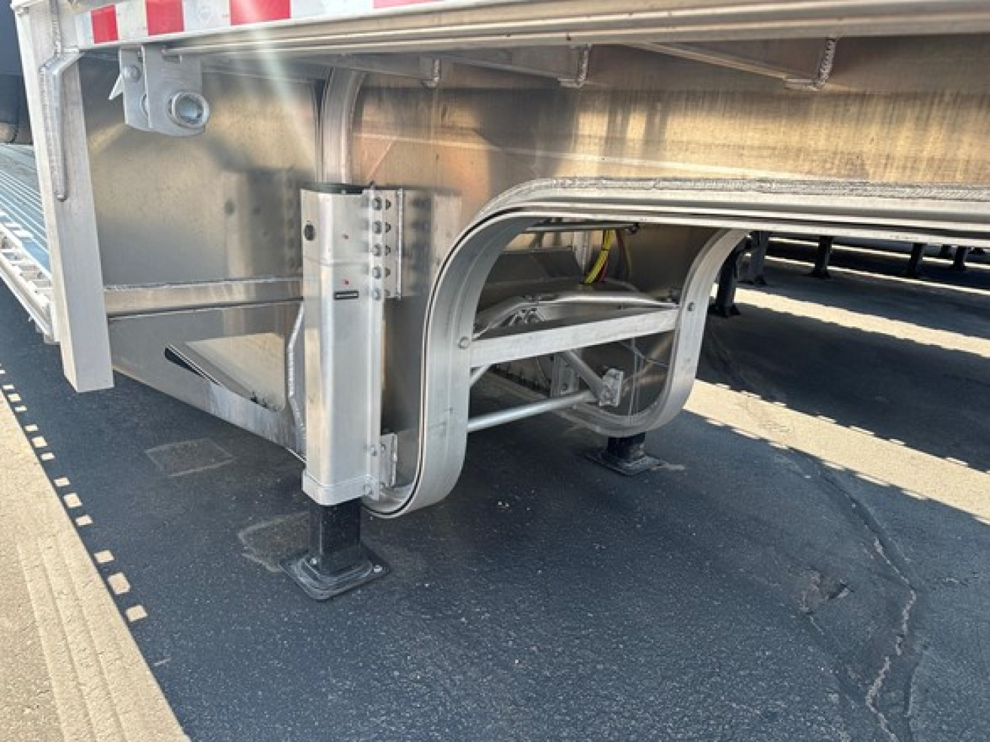 Mac drop deck trailer undercarriage showing suspension and support brackets with metal tubular frame and stabilizing jack pads.