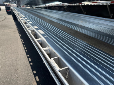 Close-up of a Mac drop deck trailer bed with ribbed aluminum surface and side guide rails.