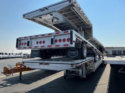 Mac drop deck trailer in raised position showing rear deck and loading ramps; aluminum flatbed with red and white reflective tape.