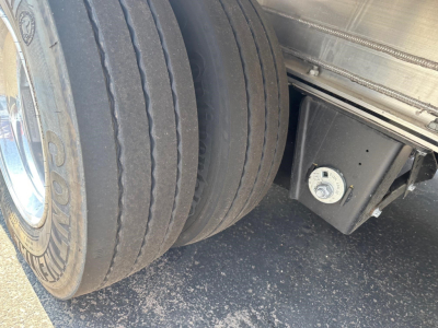 Mac drop deck trailer wheel area showing dual rear tires and underside toolbox with round gauge/bolt cap.