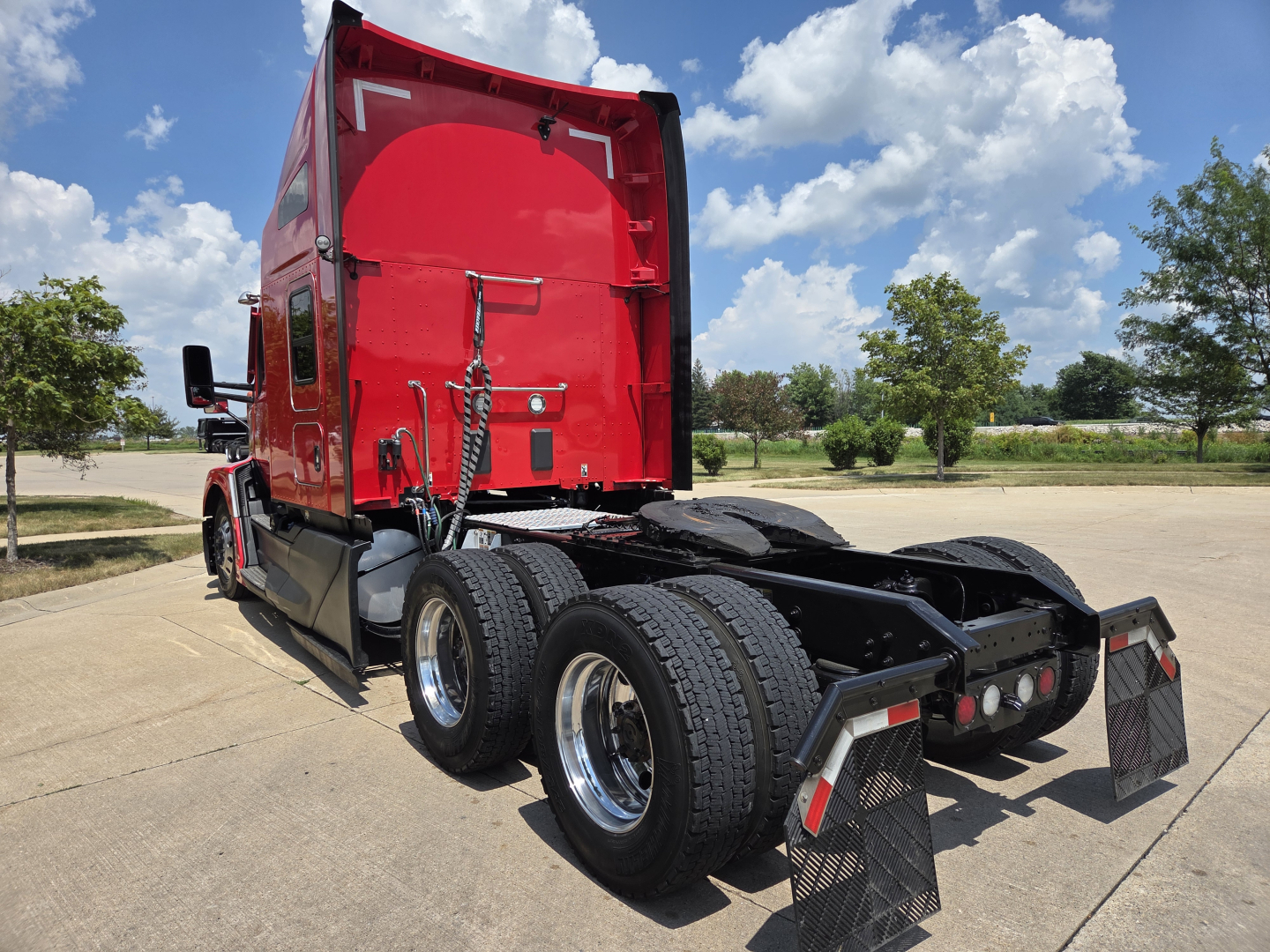 Kenworth T680 tractor rear view showing fifth wheel and dual rear axles, red sleeper cab, black chassis, fuel tanks and mud flaps