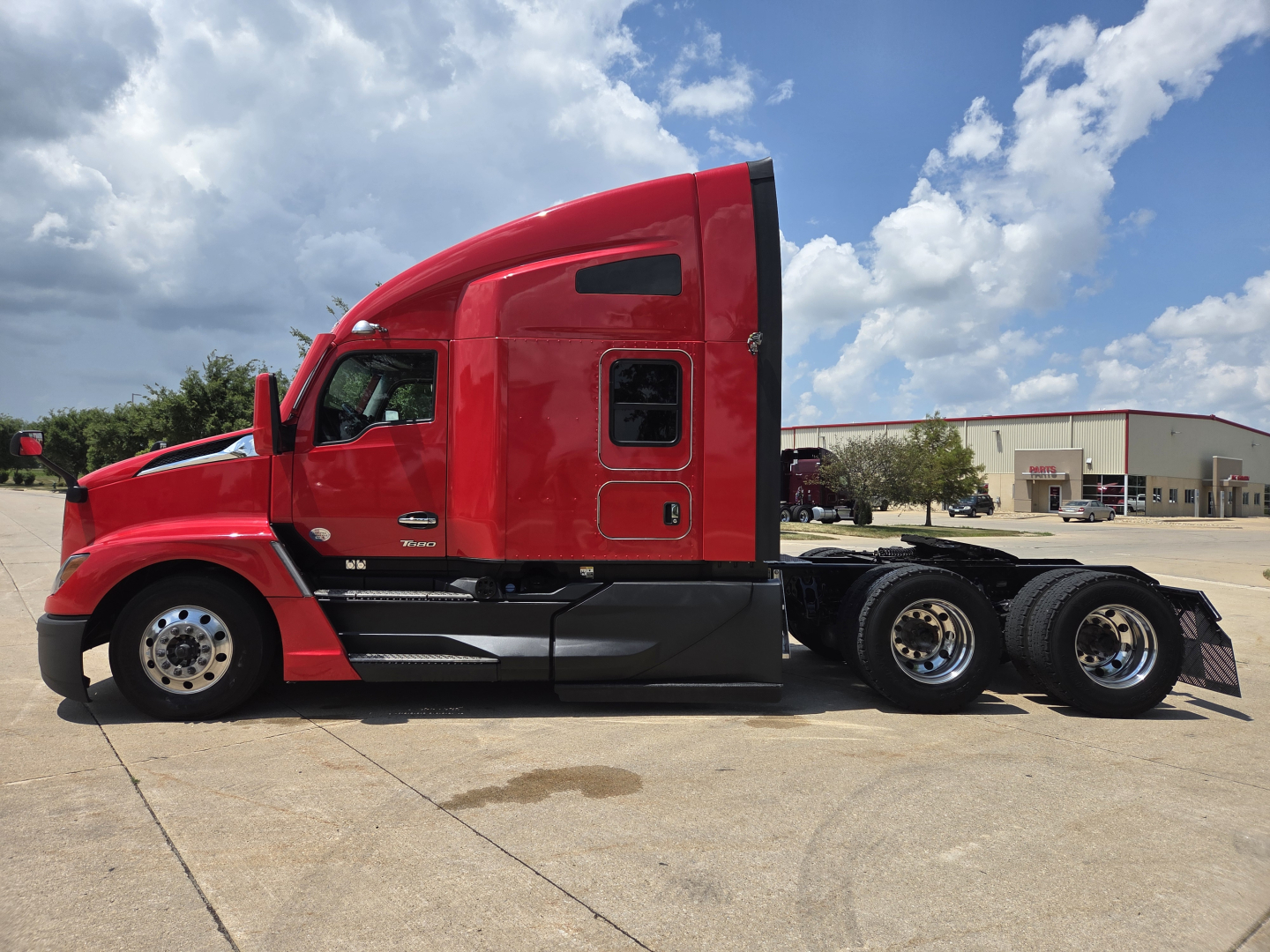 Kenworth T680 semi-truck side view showing red cab and triple rear axles.
