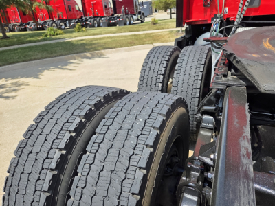 Kenworth T680 truck chassis showing dual rear axles and tires with tread pattern visible; part of cab and frame in view.