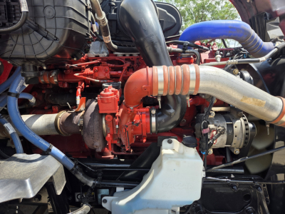 Kenworth T680 engine bay showing large red turbocharger, intake piping, hoses, and coolant reservoir.
