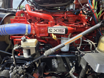 Kenworth T680 engine bay with red X15 badge, blue intercooler hose, and various hydraulic lines.