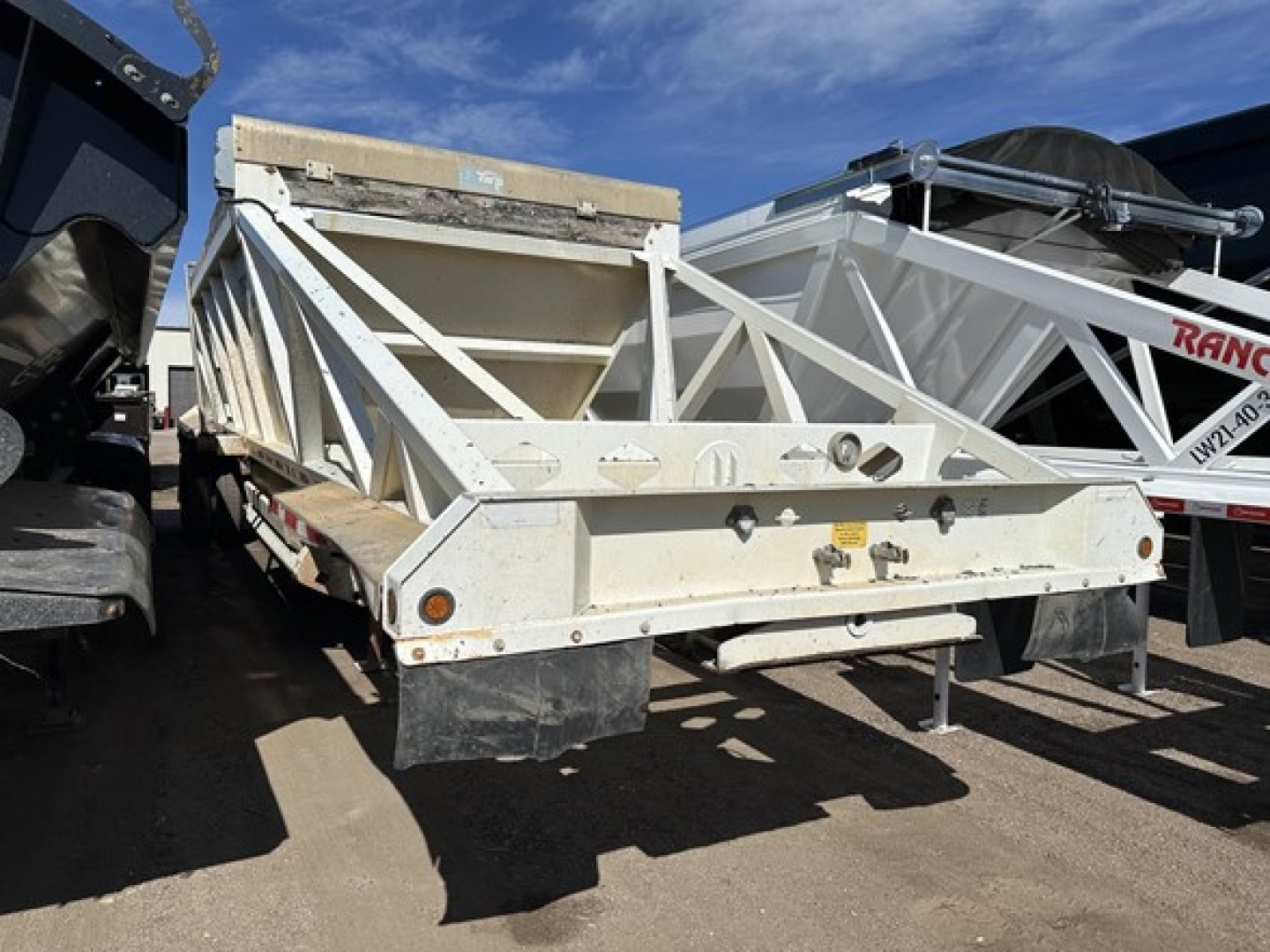 Dump trailer showing rear and side view with steel bottom and triangular frame, white paint, taillights, and bumper.
