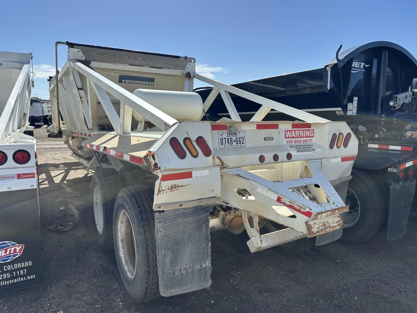 Dump trailer showing rear view with license plate area, warning sticker, and Reflective tape. Text visible includes TEXAS or state plate, UE11716 stock tag, and warning label near taillight area.