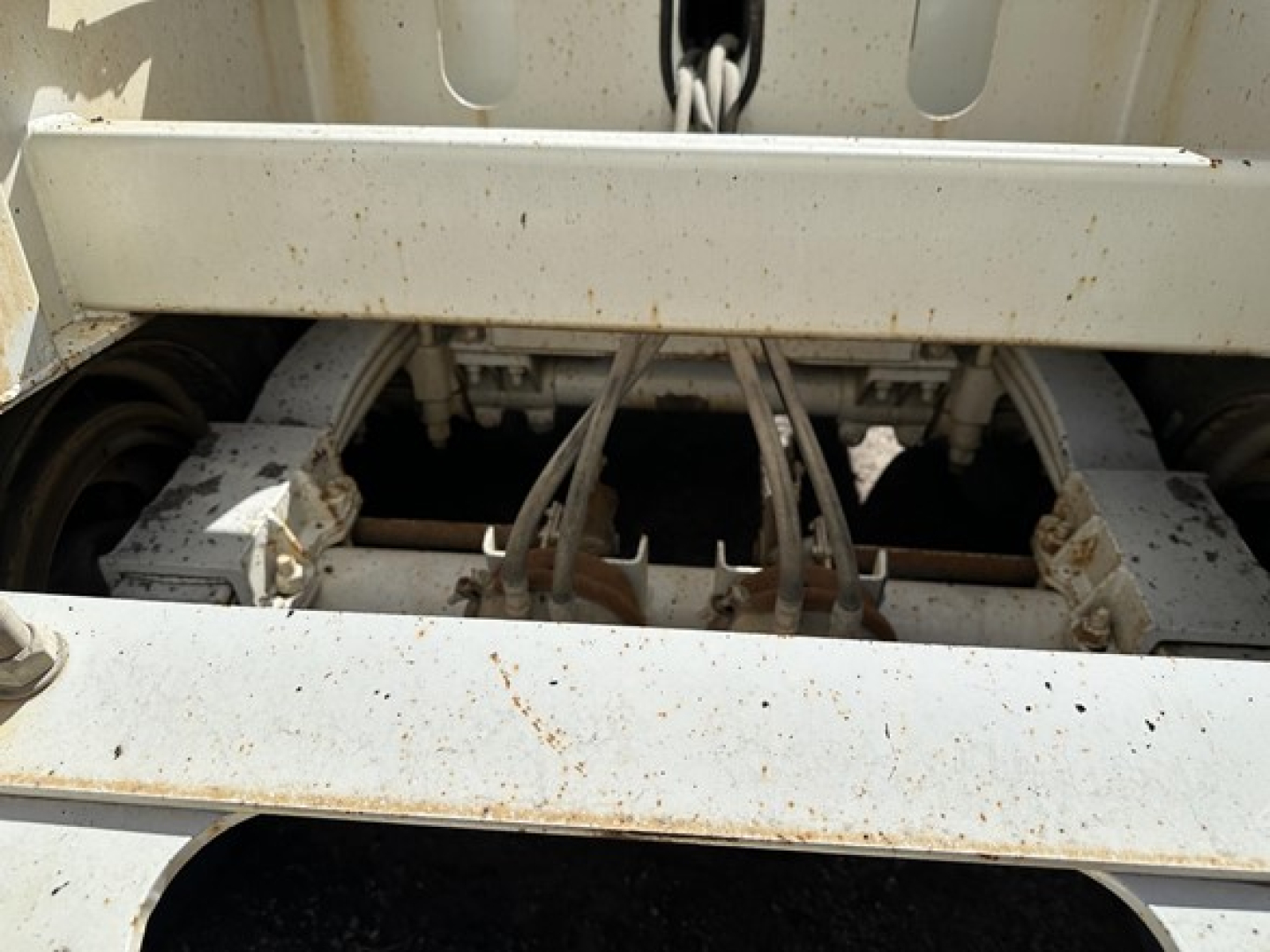 Dump trailer chassis and suspension in view showing steel frame, axles, and hydraulic hookups under a dump bed.