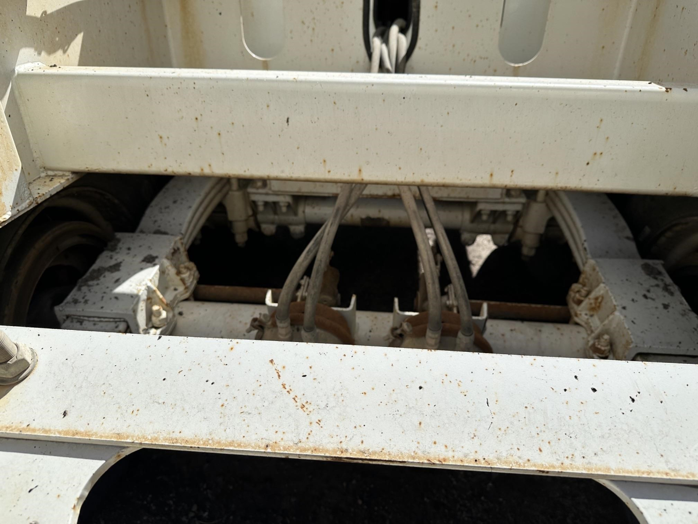 Dump trailer underside with hydraulic lines and frame components visible under a white steel bed, light rust spots on metal surface.